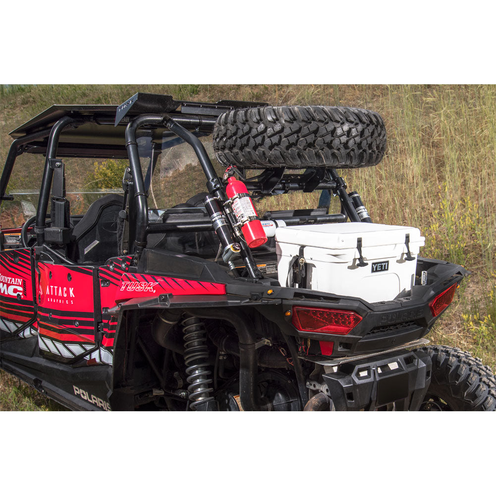A black and red Polaris RZR side-by-side utility vehicle with a roll cage, carrying a white cooler and a spare tire on a roof rack, parked outdoors in a grassy field.