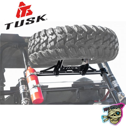Tusk brand spare tire carrier rack mounted on an off-road vehicle frame, holding a large off-road tire. A red fire extinguisher is attached to the frame.
