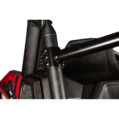 Close-up of a black metal roll bar mounting bracket attached to a tubular frame on a vehicle, with a red and black body panel visible on the left against a white background.