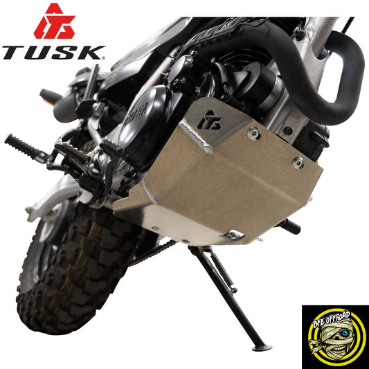 A close-up of a motorcycle engine area showing a tan metal engine guard with a TUSK logo, mounted on a black motorcycle. The TUSK logo is also displayed in the top-left corner, and a BFE Offroad logo sticker is shown in the bottom-right corner.