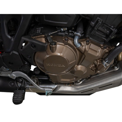 Close-up of a motorcycle engine cover with a metallic bronze Honda logo, surrounded by black and silver mechanical parts on a white background.