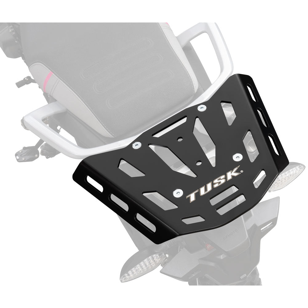 A black TUSK motorcycle rear luggage rack with cutout slots and silver hardware, shown mounted on a white motorcycle against a light gray background.