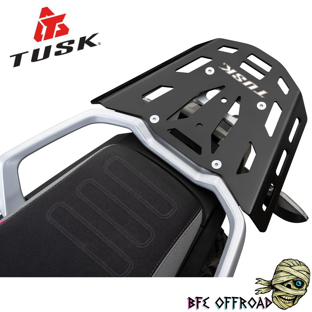 A black metal luggage rack with silver mounting brackets, shown installed on a motorcycle seat. The TUSK brand logo is visible on the rack and in the top-left corner, with a BFE OFFROAD logo in the bottom-right corner.