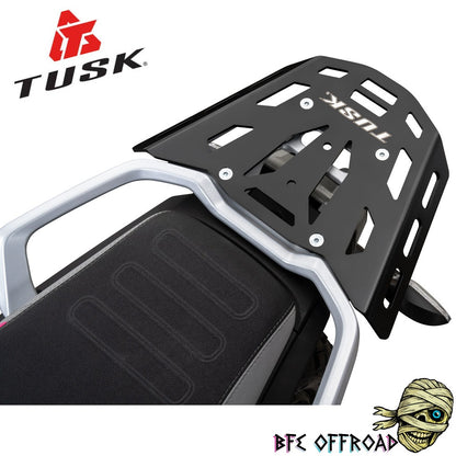 A black metal luggage rack with silver mounting brackets, shown installed on a motorcycle seat. The TUSK brand logo is visible on the rack and in the top-left corner, with a BFE OFFROAD logo in the bottom-right corner.