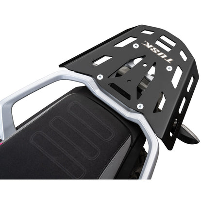 A black metal luggage rack mounted behind a motorcycle seat, shown on a clean white background. The rack features the brand name 'TUSK' in white lettering.