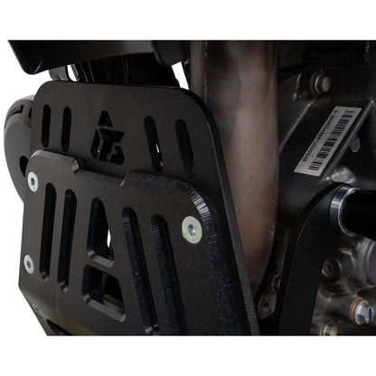 Close-up of a black metal engine guard or skid plate mounted over a motorcycle or ATV engine, with visible screws and part of the engine components behind it.